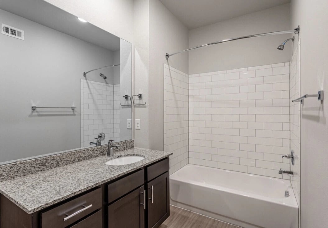 Bathroom in an apartment unit with granite vanity, dark cabinetry, and white subway-tiled tub/shower.