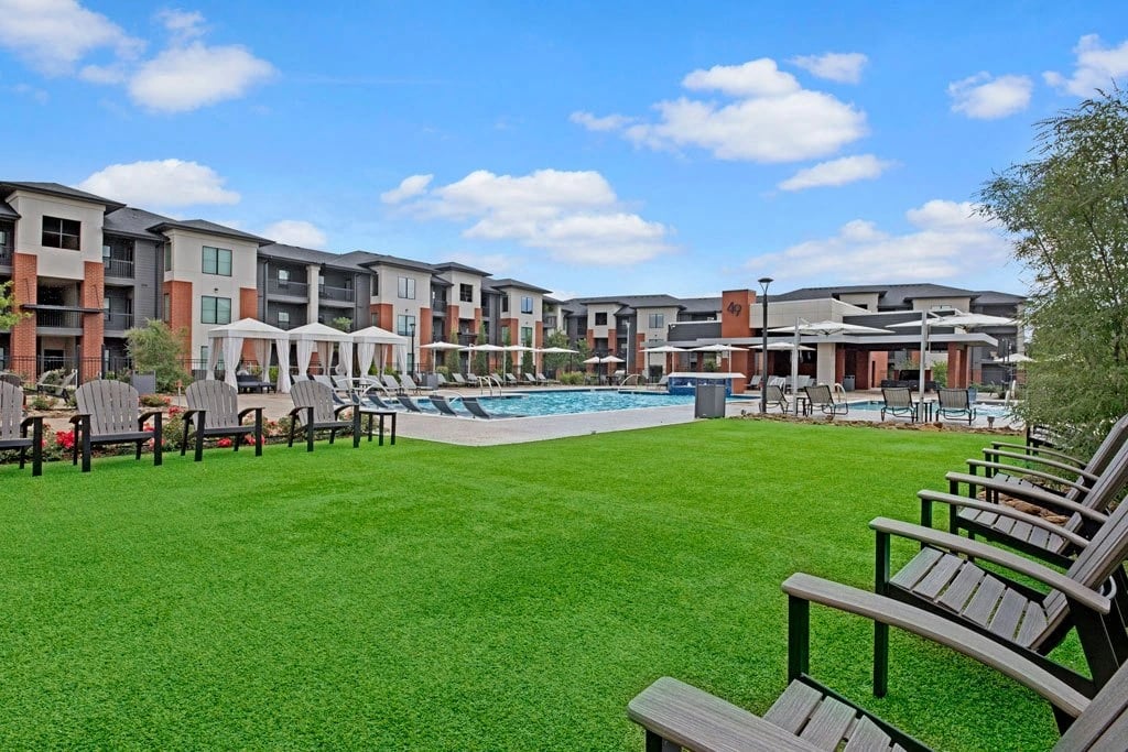 Outdoor apartment community pool area with lounge chairs, cabanas, and manicured lawn.
