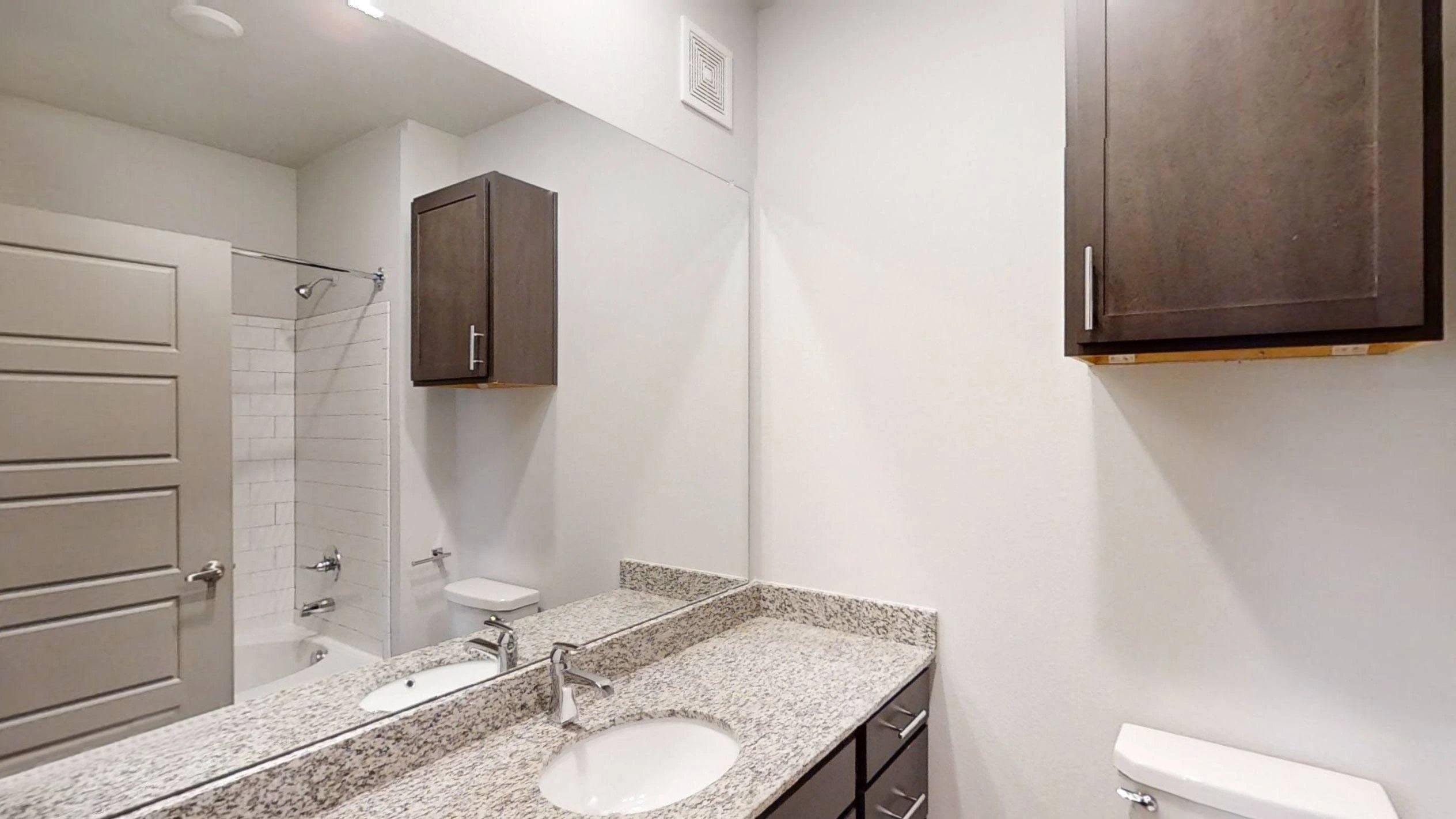Bathroom vanity with granite countertop, dual sinks, mirror, and storage cabinets; toilet and bathtub/shower visible.