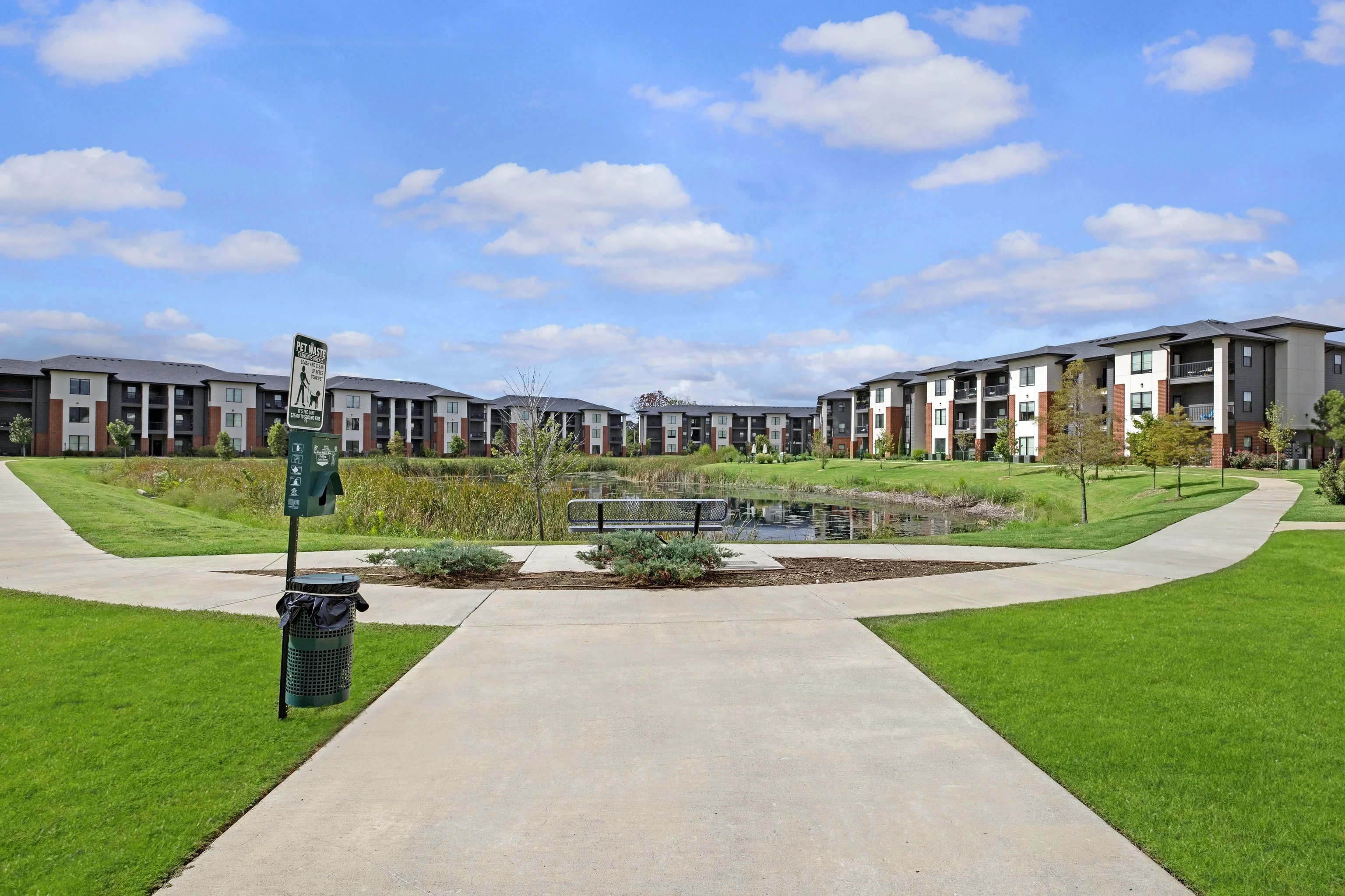 Exterior view of a modern apartment community with a pond and walking paths.