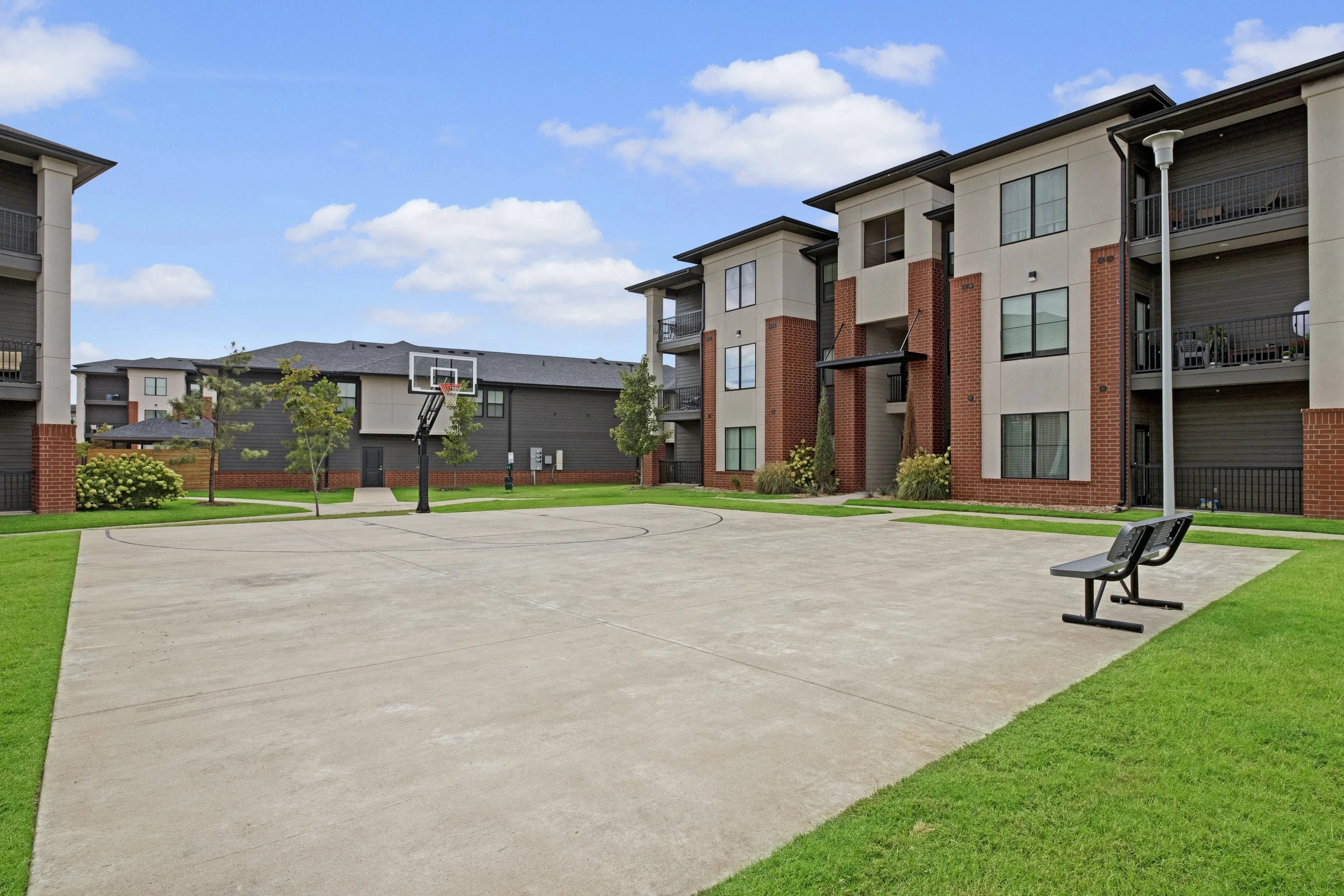 Outdoor community courtyard with a basketball court, benches, and apartment buildings.