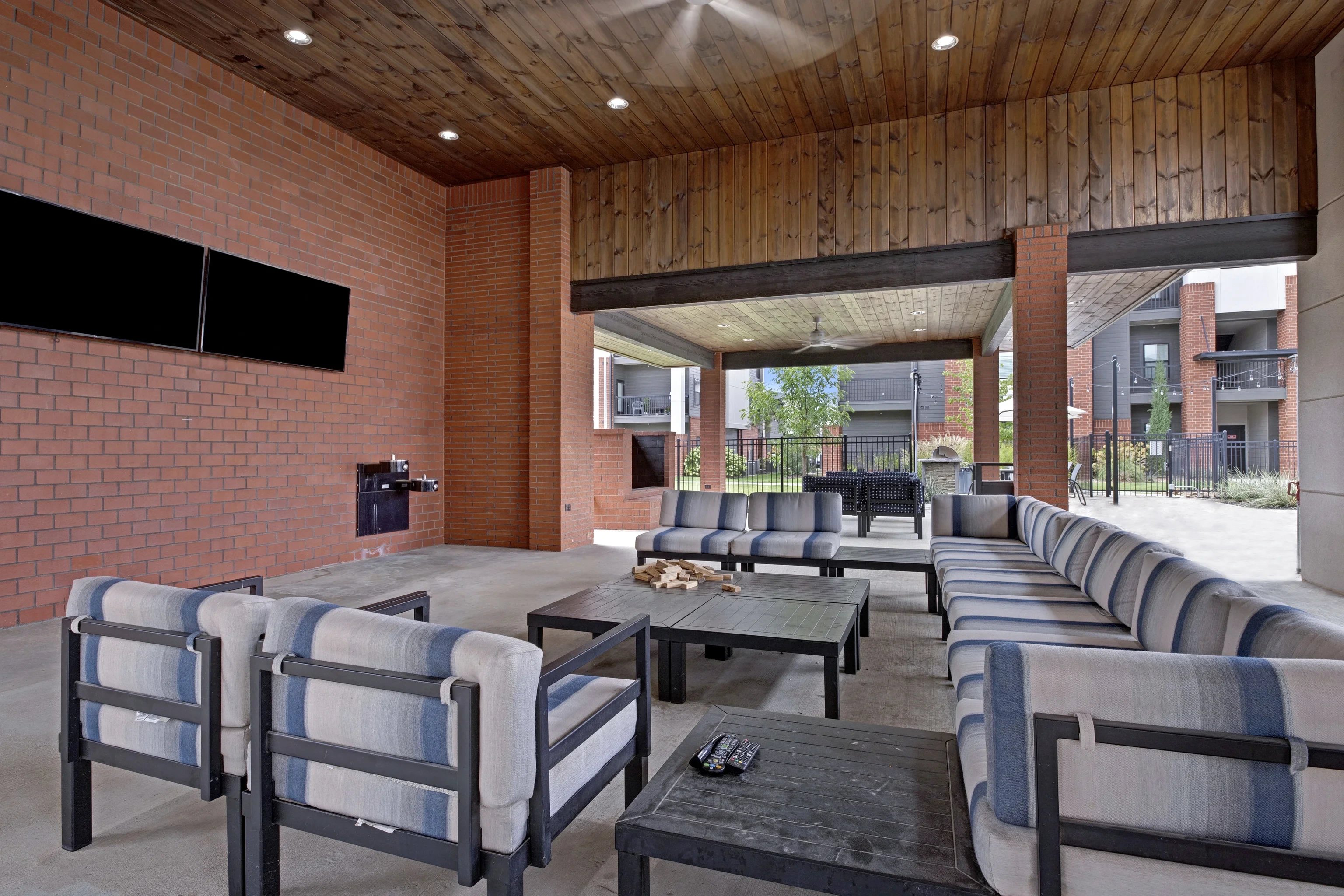 Outdoor covered community lounge with cushioned seating and wall-mounted TVs.