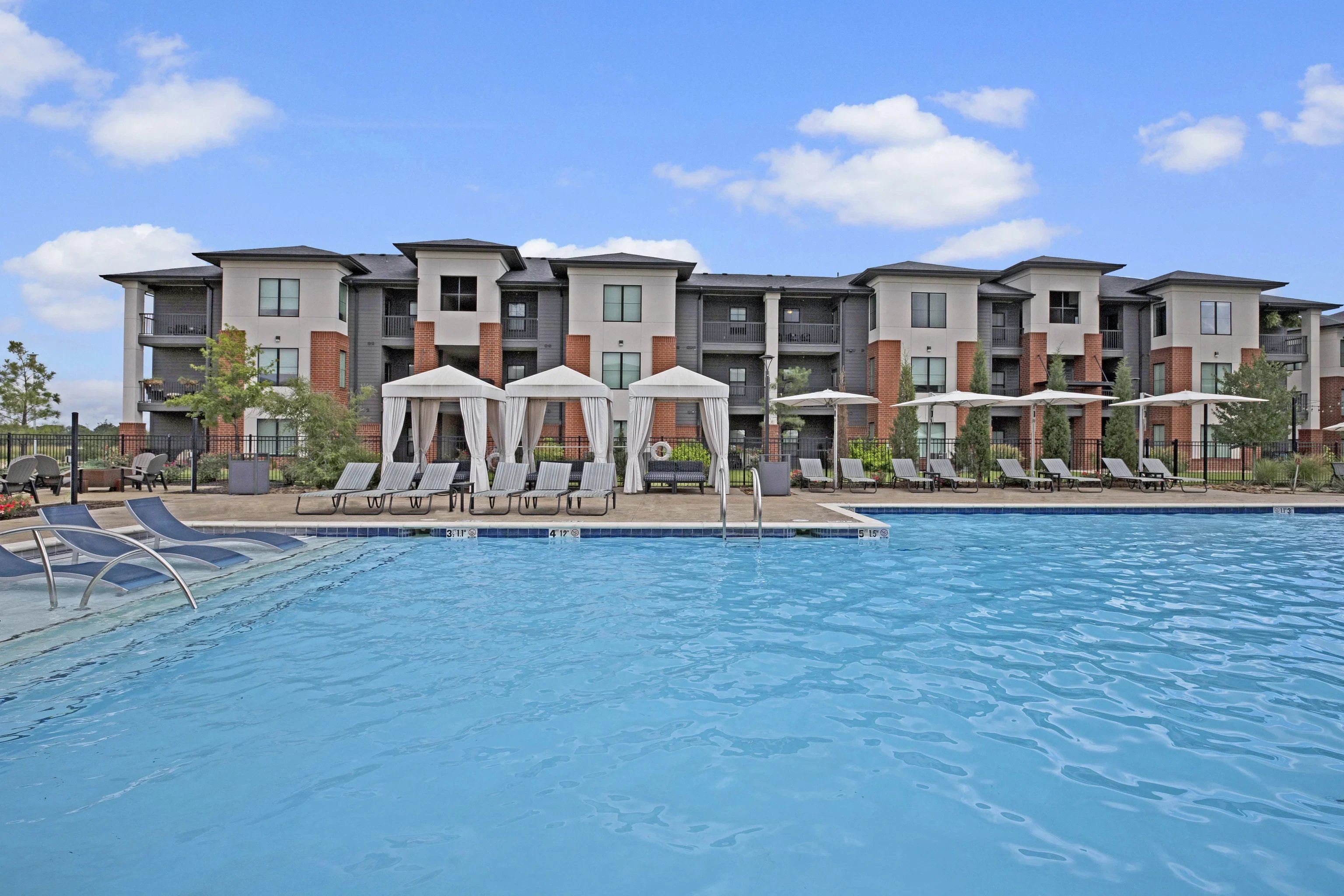 Outdoor pool scene at an apartment community with lounge chairs and cabanas.