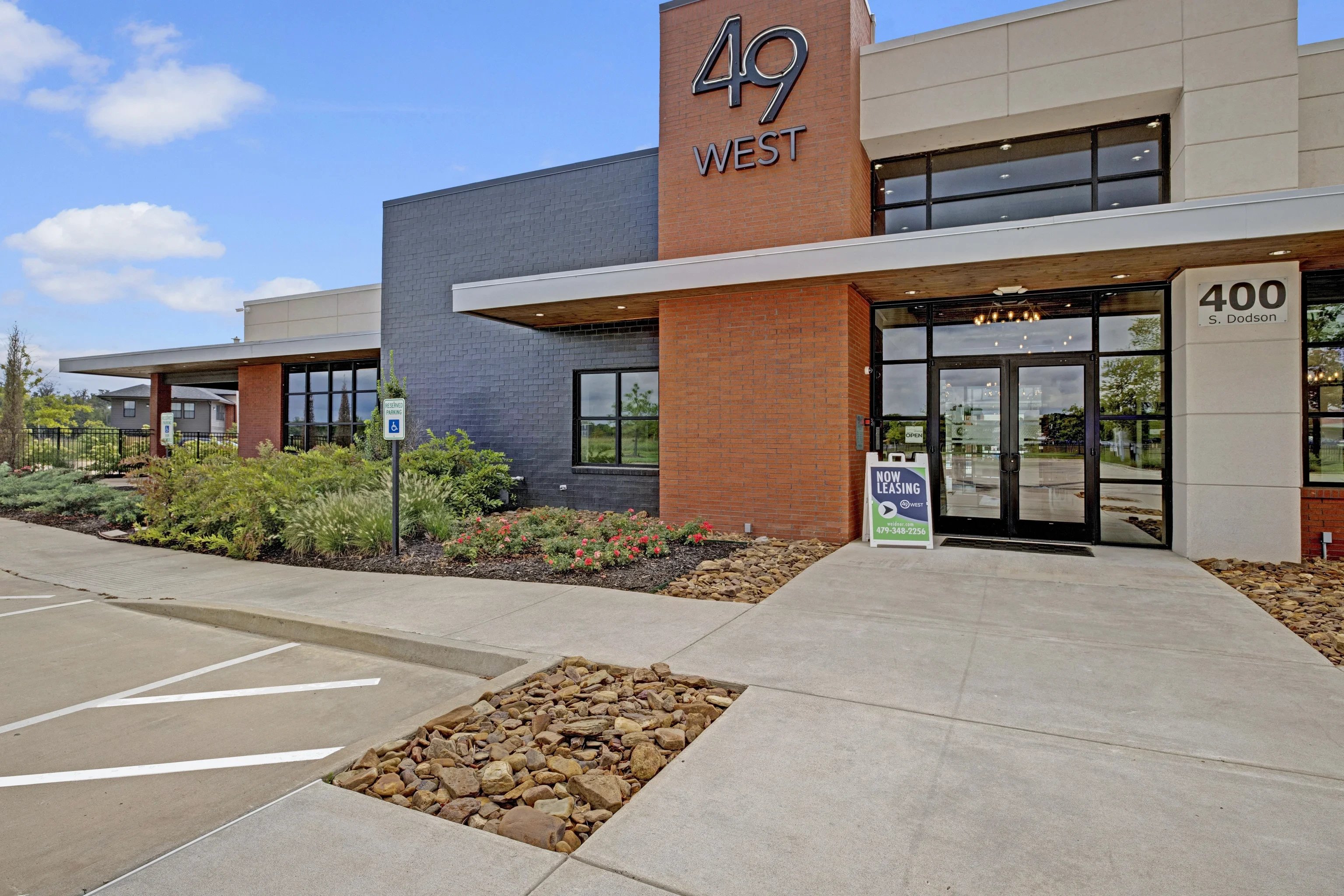 Exterior view of the 49 West apartment community entrance with Now Leasing sign and parking.