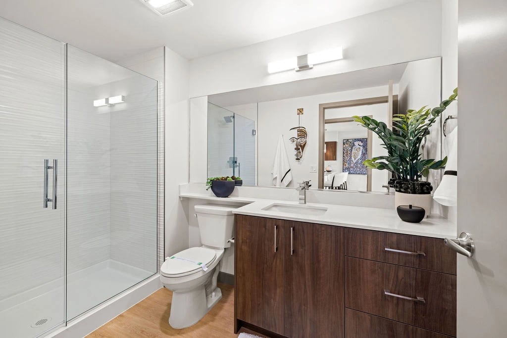 Modern apartment bathroom with glass-enclosed shower, white countertop, and dark wood vanity.