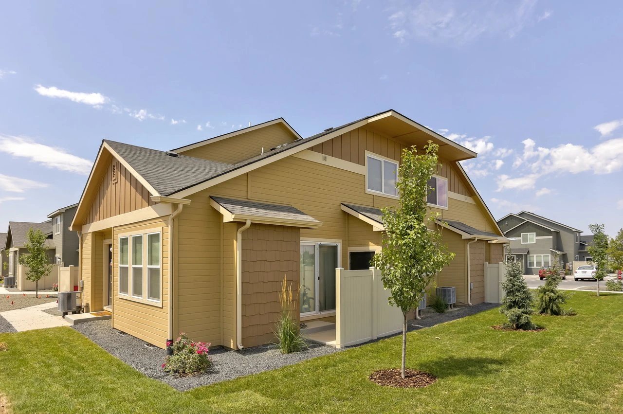 Exterior view of tan townhomes with green lawns and blue sky.