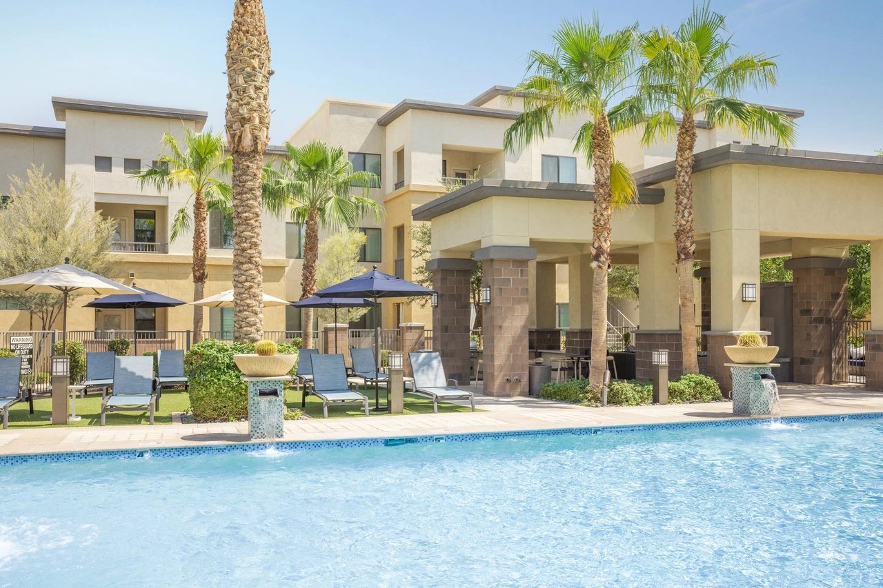 Resort-style swimming pool with lounge chairs and palm trees at an apartment complex.