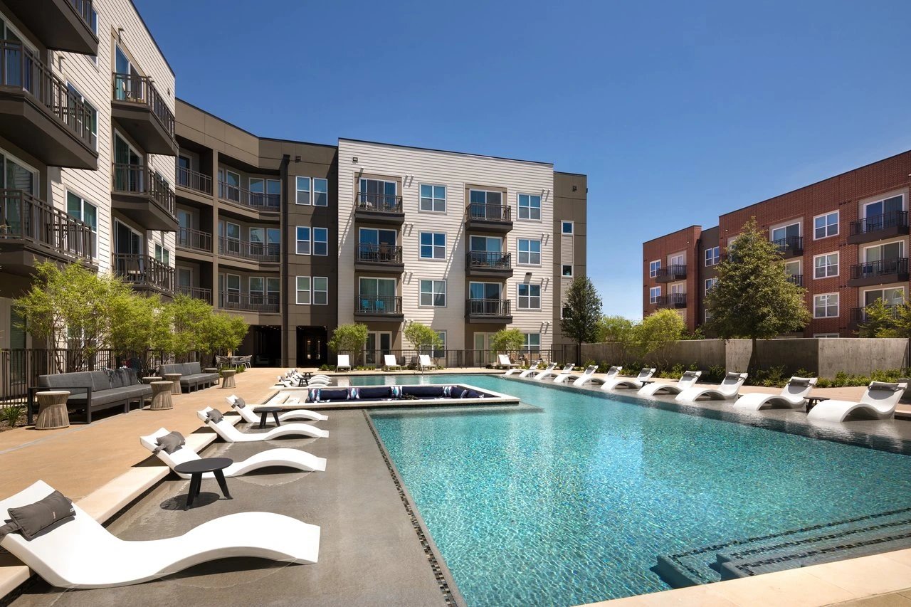 Modern swimming pool with lounge chairs and seating areas in front of apartment buildings.