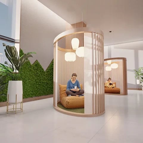 Two people sit in circular pod seating in a bright modern lobby with plants.